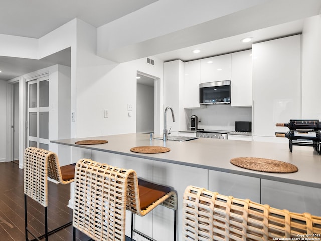 kitchen with kitchen peninsula, dark hardwood / wood-style flooring, a breakfast bar, sink, and white cabinetry