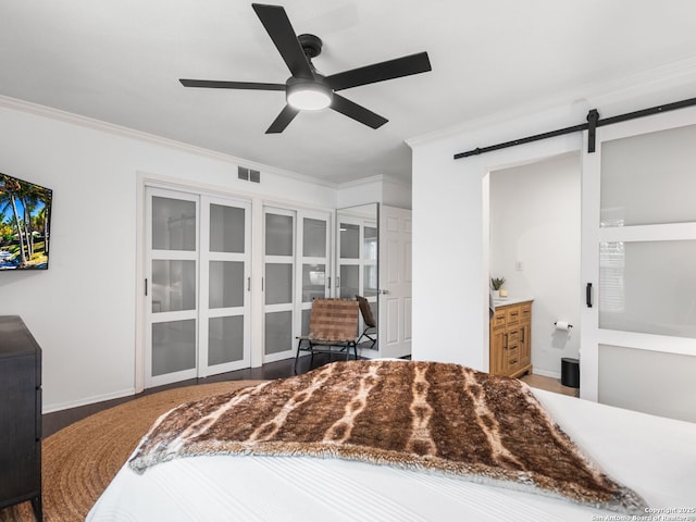 bedroom featuring ceiling fan, connected bathroom, a barn door, and crown molding