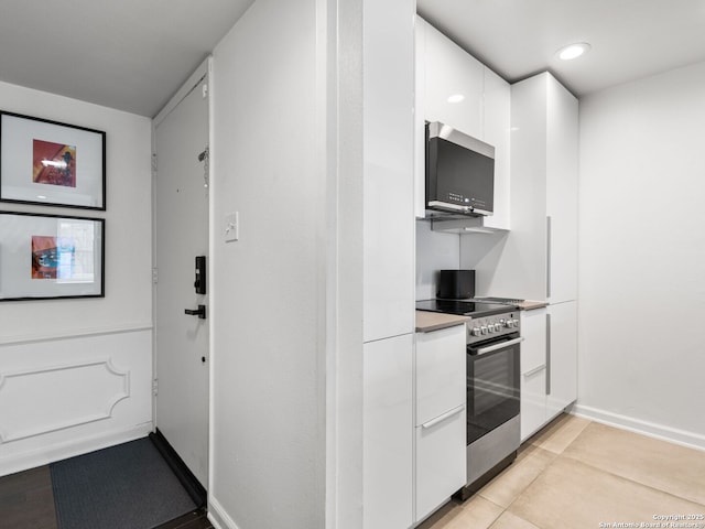 kitchen featuring stainless steel electric stove, light tile patterned flooring, and white cabinetry