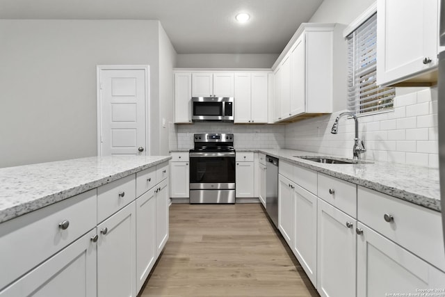 kitchen with light stone counters, stainless steel appliances, light wood-type flooring, white cabinetry, and sink