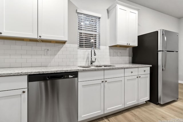 kitchen featuring white cabinetry, stainless steel appliances, light stone counters, sink, and light hardwood / wood-style flooring