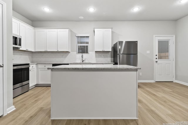 kitchen featuring light stone counters, a center island, stainless steel appliances, white cabinets, and sink