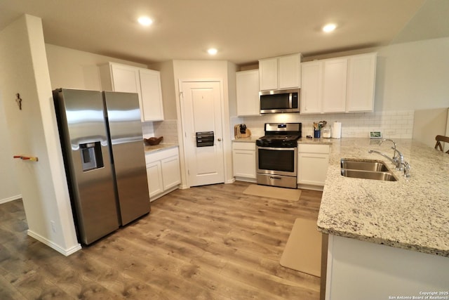 kitchen featuring light stone counters, stainless steel appliances, light hardwood / wood-style floors, white cabinetry, and sink