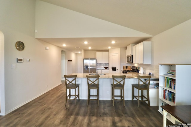 kitchen with vaulted ceiling, stainless steel appliances, light stone counters, decorative backsplash, and white cabinets