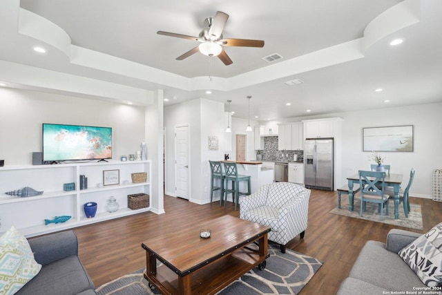 living room featuring dark hardwood / wood-style flooring, ceiling fan, and a raised ceiling