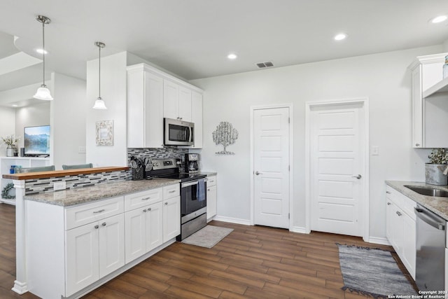 kitchen with kitchen peninsula, hanging light fixtures, decorative backsplash, white cabinetry, and appliances with stainless steel finishes