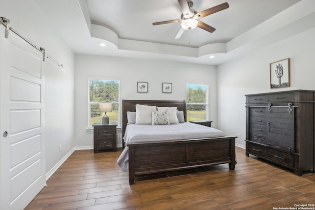 bedroom with a raised ceiling, ceiling fan, and a barn door