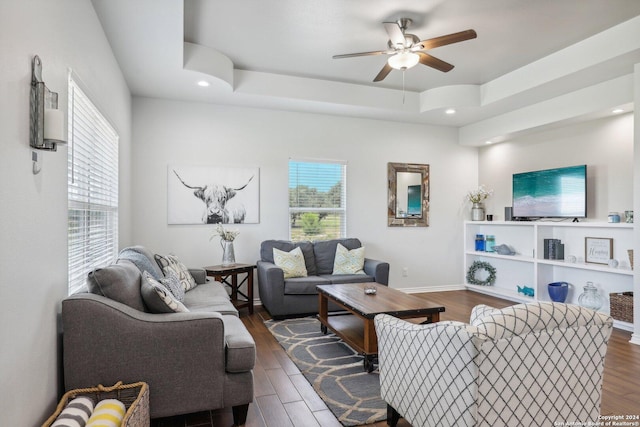 living room with dark hardwood / wood-style flooring, ceiling fan, and a tray ceiling