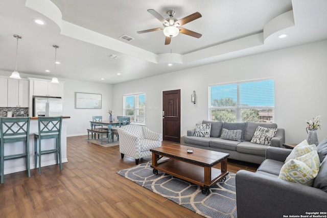 living room with a raised ceiling, ceiling fan, and dark wood-type flooring