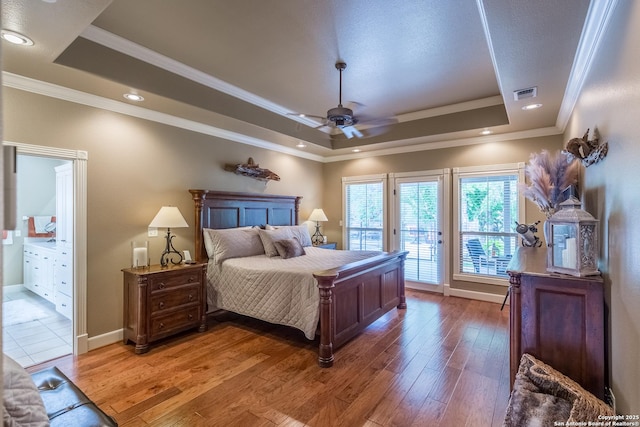 bedroom featuring connected bathroom, hardwood / wood-style floors, a tray ceiling, ceiling fan, and access to exterior