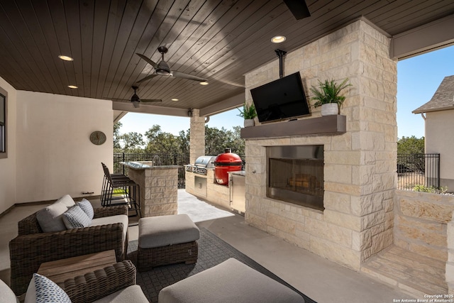 view of patio / terrace with an outdoor stone fireplace, an outdoor kitchen, a bar, area for grilling, and ceiling fan