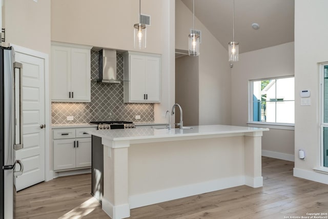 kitchen featuring white cabinetry, hanging light fixtures, an island with sink, and wall chimney exhaust hood