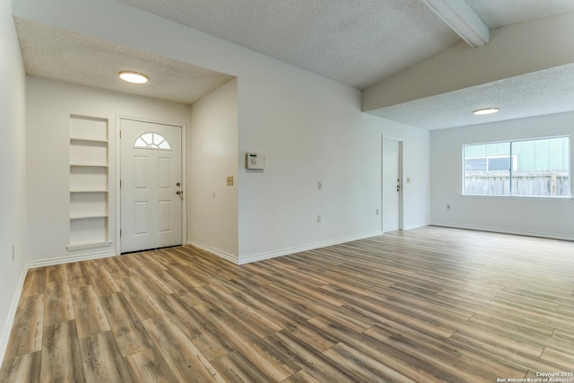 foyer with wood-type flooring, a textured ceiling, and lofted ceiling with beams