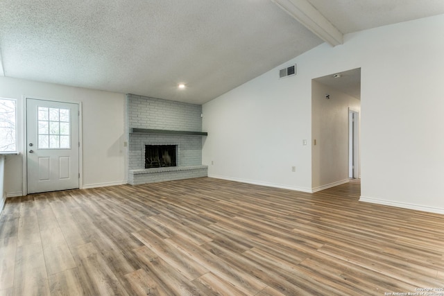 unfurnished living room featuring light hardwood / wood-style floors, a brick fireplace, lofted ceiling with beams, and a textured ceiling