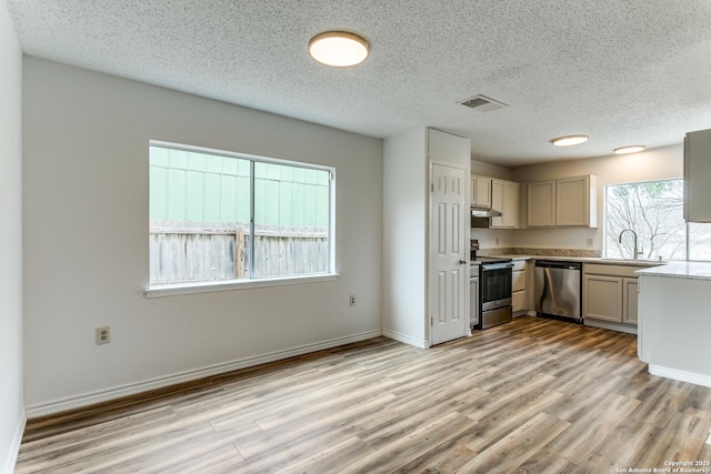 kitchen with a textured ceiling, appliances with stainless steel finishes, light hardwood / wood-style floors, and sink