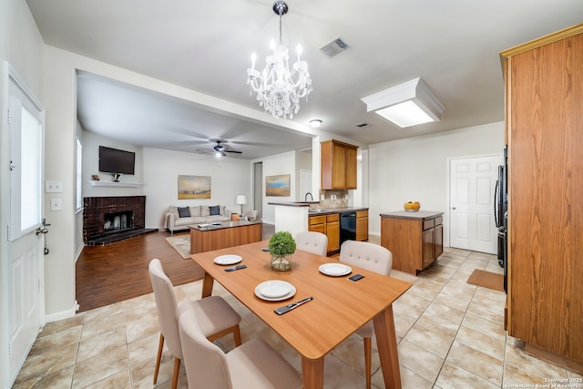 tiled dining room featuring ceiling fan with notable chandelier, a brick fireplace, and sink