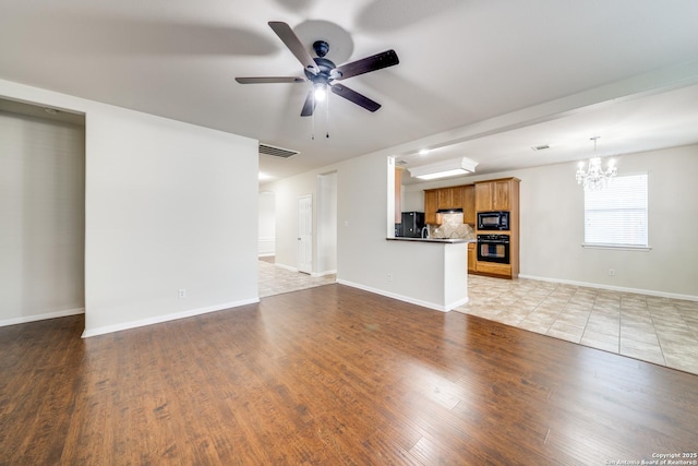 unfurnished living room with ceiling fan with notable chandelier and light hardwood / wood-style floors