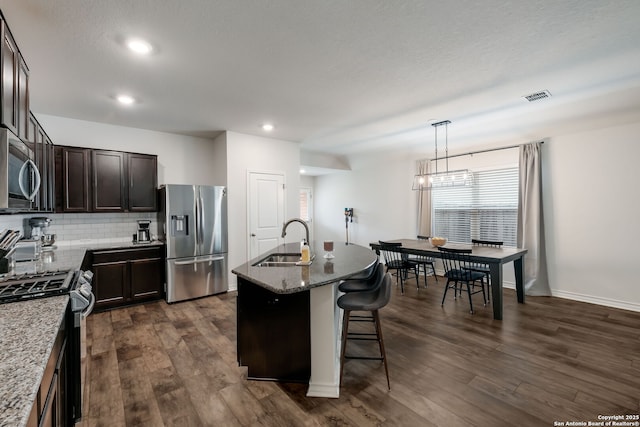 kitchen featuring hanging light fixtures, stainless steel appliances, a kitchen island with sink, stone countertops, and sink