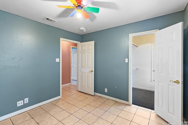 unfurnished bedroom featuring a closet, ceiling fan, light tile patterned floors, and a spacious closet