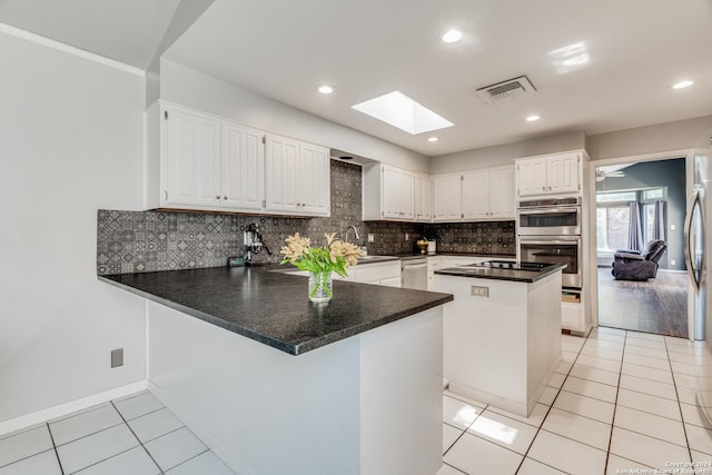 kitchen featuring white cabinetry, ceiling fan, kitchen peninsula, a skylight, and appliances with stainless steel finishes