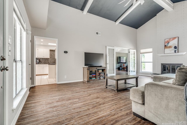 living room with beamed ceiling, a brick fireplace, high vaulted ceiling, and wood-type flooring