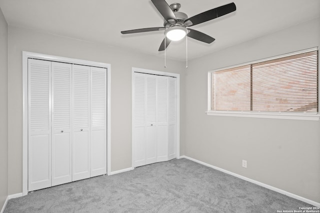 unfurnished bedroom featuring two closets, ceiling fan, and light carpet