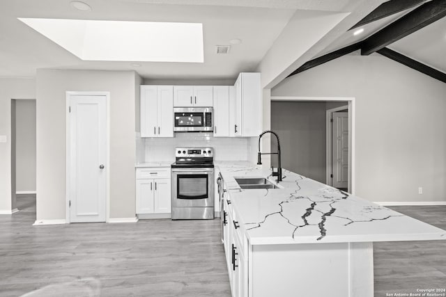 kitchen featuring sink, appliances with stainless steel finishes, lofted ceiling with skylight, and white cabinetry