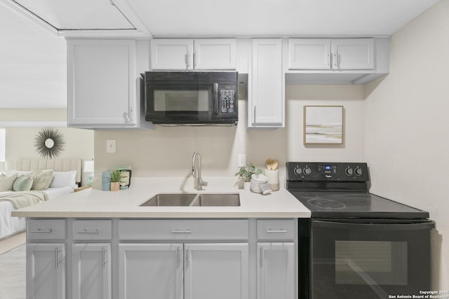 kitchen with black appliances, white cabinetry, light countertops, and a sink