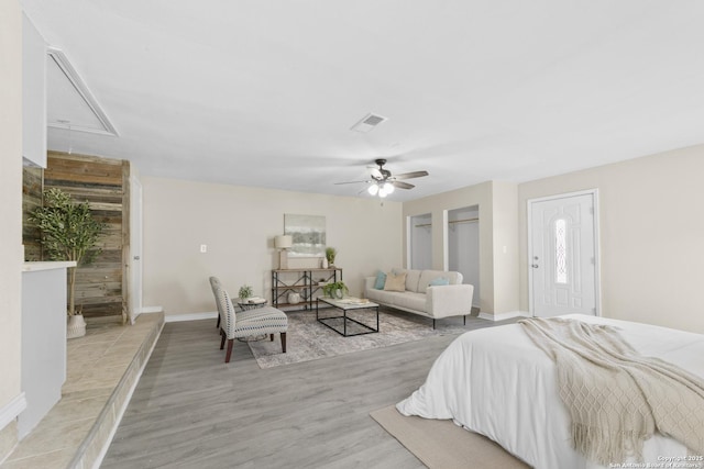 bedroom with ceiling fan, light wood-style flooring, visible vents, baseboards, and attic access