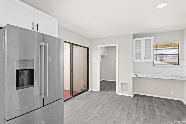 kitchen featuring light wood-type flooring, light stone counters, decorative backsplash, stainless steel refrigerator with ice dispenser, and white cabinets