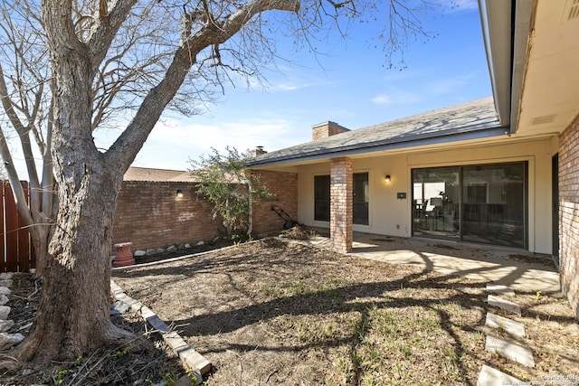 exterior space featuring a patio area, fence, a chimney, and brick siding