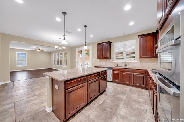 kitchen with appliances with stainless steel finishes, hanging light fixtures, a kitchen island, sink, and ceiling fan with notable chandelier