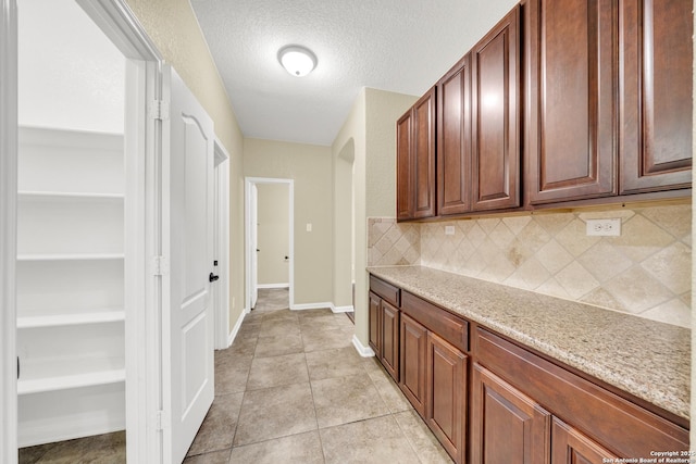 kitchen featuring light stone counters, a textured ceiling, light tile patterned flooring, and tasteful backsplash