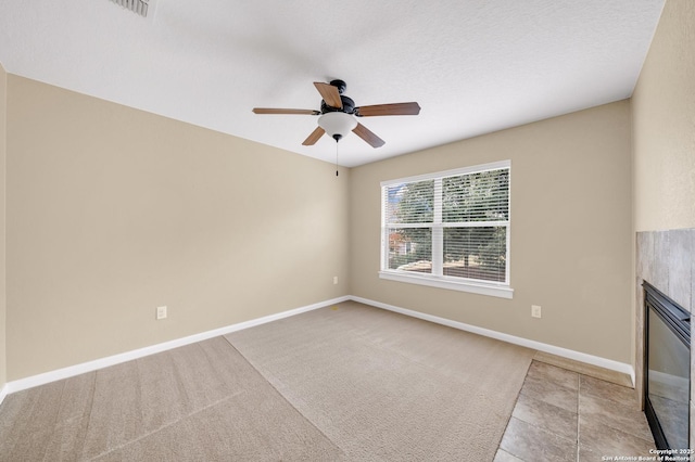 empty room featuring a tiled fireplace, ceiling fan, and light tile patterned flooring