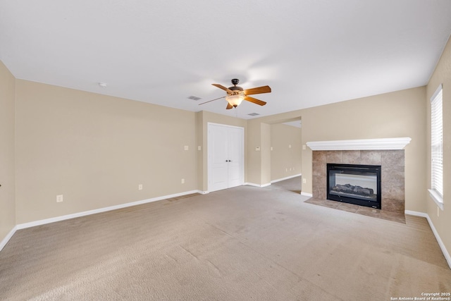 unfurnished living room featuring a tiled fireplace, ceiling fan, and carpet