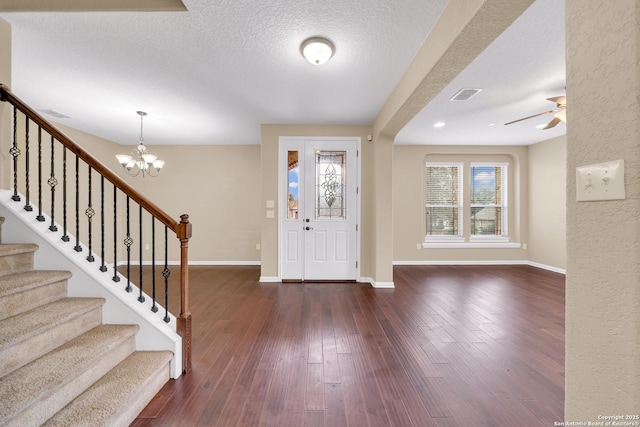 foyer with ceiling fan with notable chandelier, a textured ceiling, and dark hardwood / wood-style flooring