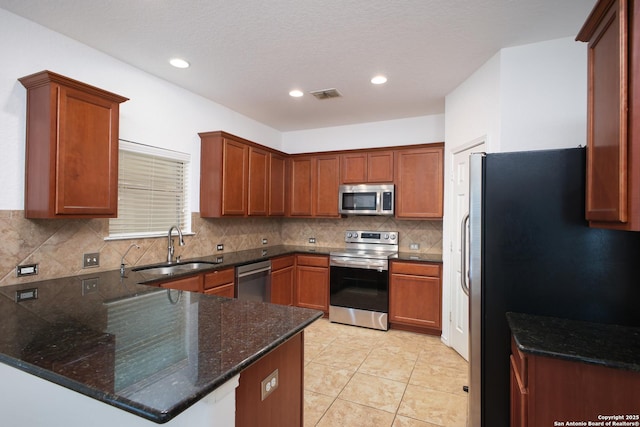 kitchen with sink, dark stone countertops, light tile patterned floors, kitchen peninsula, and appliances with stainless steel finishes