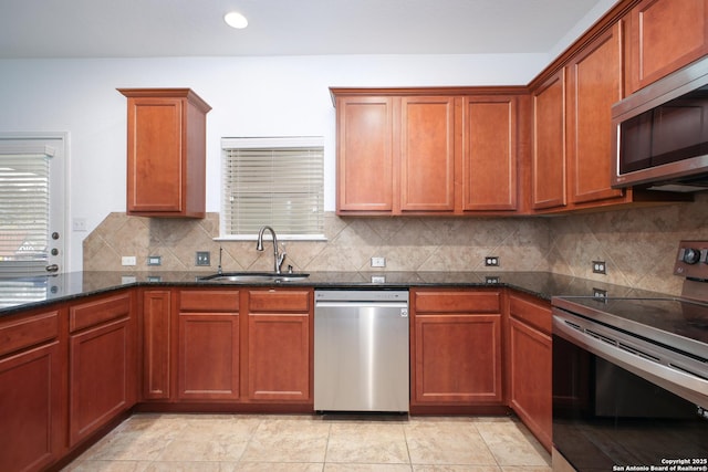 kitchen with sink, dark stone countertops, light tile patterned floors, decorative backsplash, and appliances with stainless steel finishes