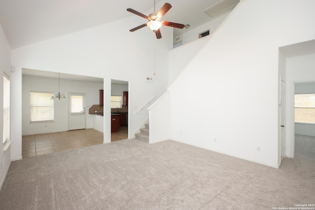 unfurnished living room with light colored carpet, high vaulted ceiling, and ceiling fan with notable chandelier