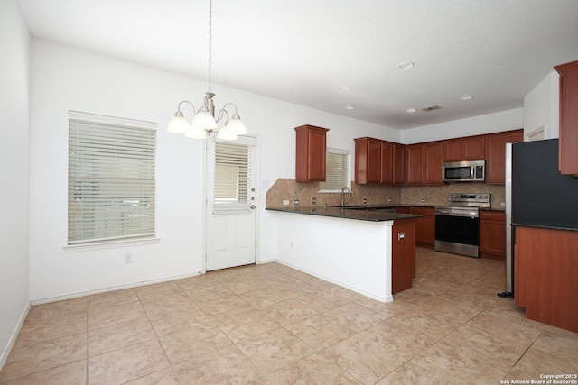 kitchen with appliances with stainless steel finishes, kitchen peninsula, pendant lighting, sink, and an inviting chandelier