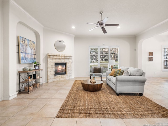 living room featuring ceiling fan, ornamental molding, a fireplace, and light tile patterned floors