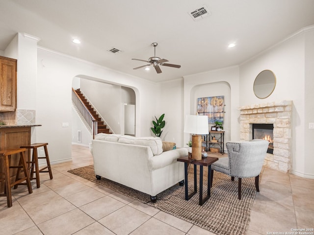 tiled living room featuring a fireplace, ceiling fan, and ornamental molding