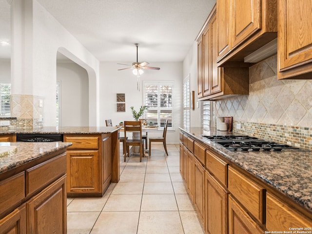 kitchen with dark stone countertops, gas stovetop, backsplash, and plenty of natural light