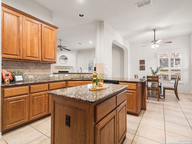 kitchen featuring kitchen peninsula, light tile patterned floors, dark stone counters, decorative backsplash, and a kitchen island