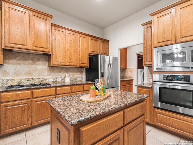 kitchen with appliances with stainless steel finishes, dark stone counters, a center island, and decorative backsplash