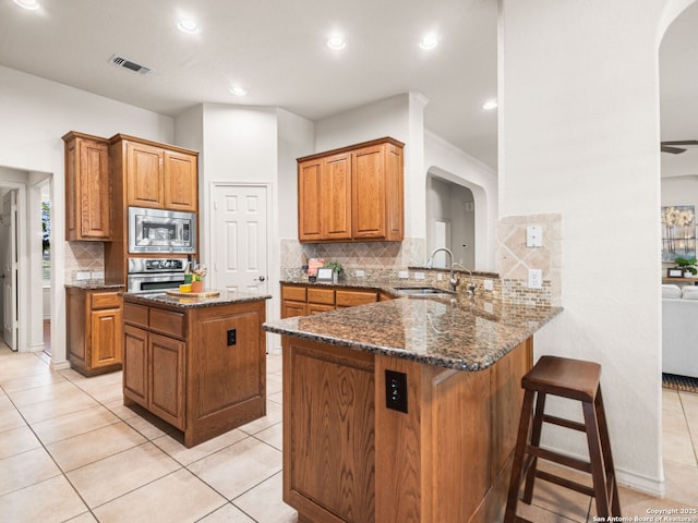 kitchen featuring dark stone countertops, stainless steel appliances, kitchen peninsula, light tile patterned floors, and sink