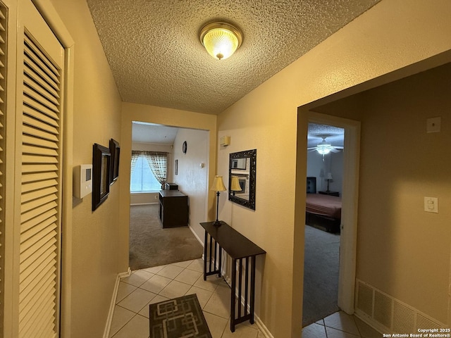 hallway with a textured ceiling and light tile patterned floors