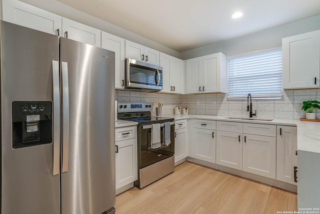 kitchen featuring light stone counters, light hardwood / wood-style flooring, stainless steel appliances, white cabinetry, and sink