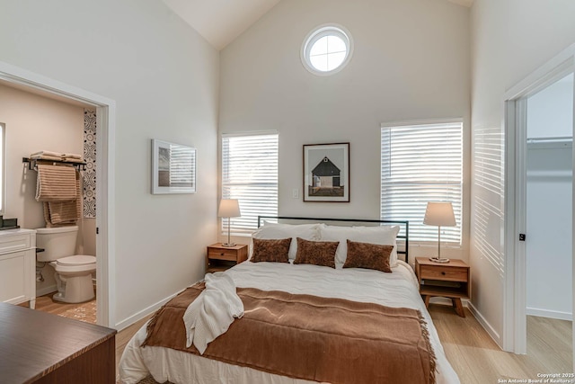 bedroom with ensuite bath, high vaulted ceiling, light hardwood / wood-style floors, and a spacious closet