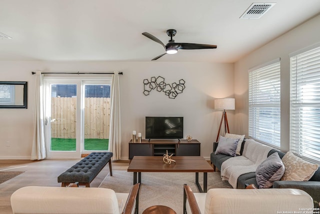 living room with light wood-type flooring, ceiling fan, and a healthy amount of sunlight